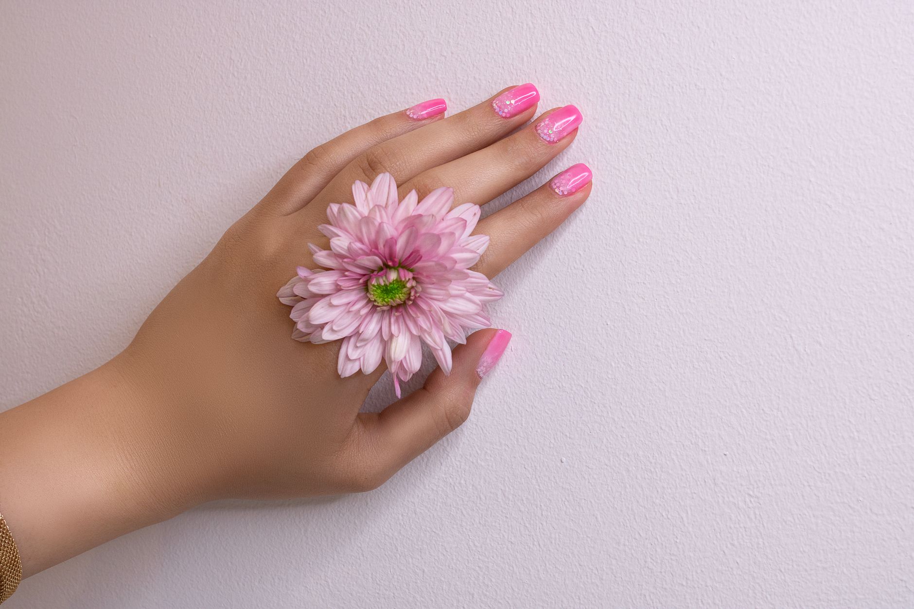 Une main féminine avec un nail art en dégradé rose et blanc tenant une fleur rose sur un fond clair.