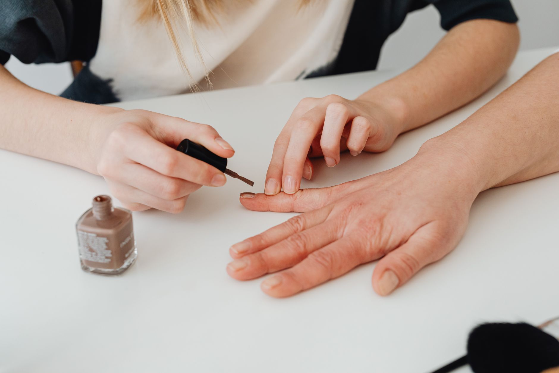 Une personne applique du vernis à ongles marron sur les ongles d'une autre personne.