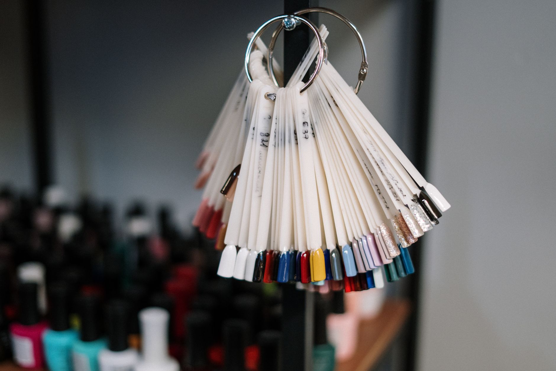 Un nuancier d'ongles en éventail suspendu devant une collection de flacons de vernis à ongles colorés.