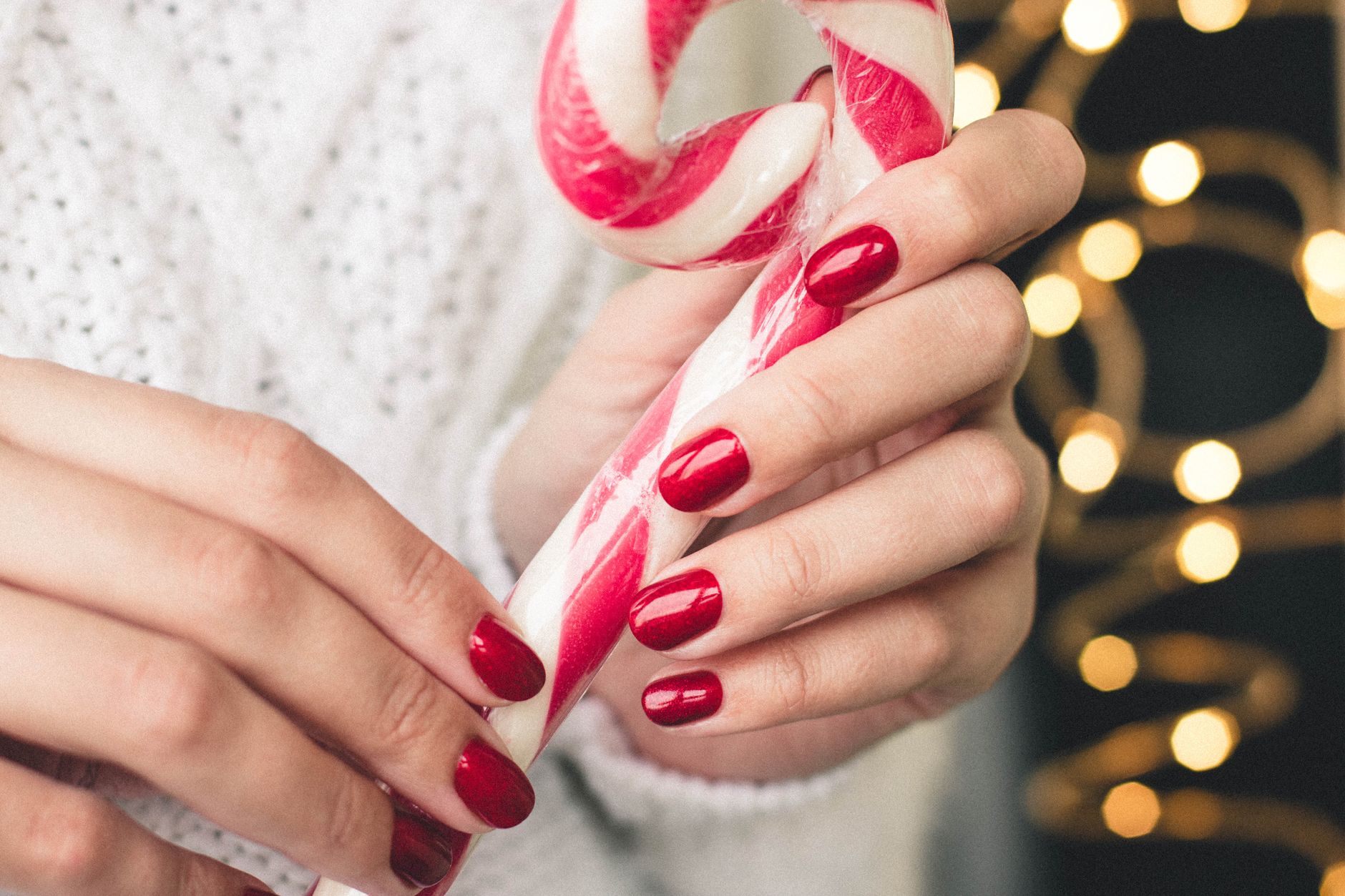 Main aux ongles rouges tenant un sucre d'orge rouge et blanc