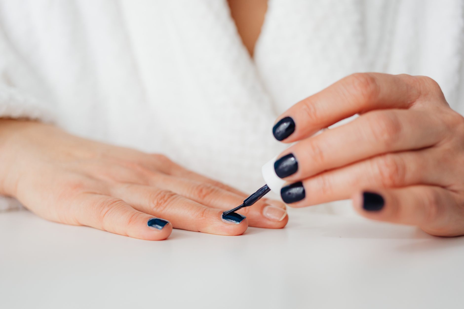 Une femme applique du vernis à ongles bleu foncé sur ses ongles.